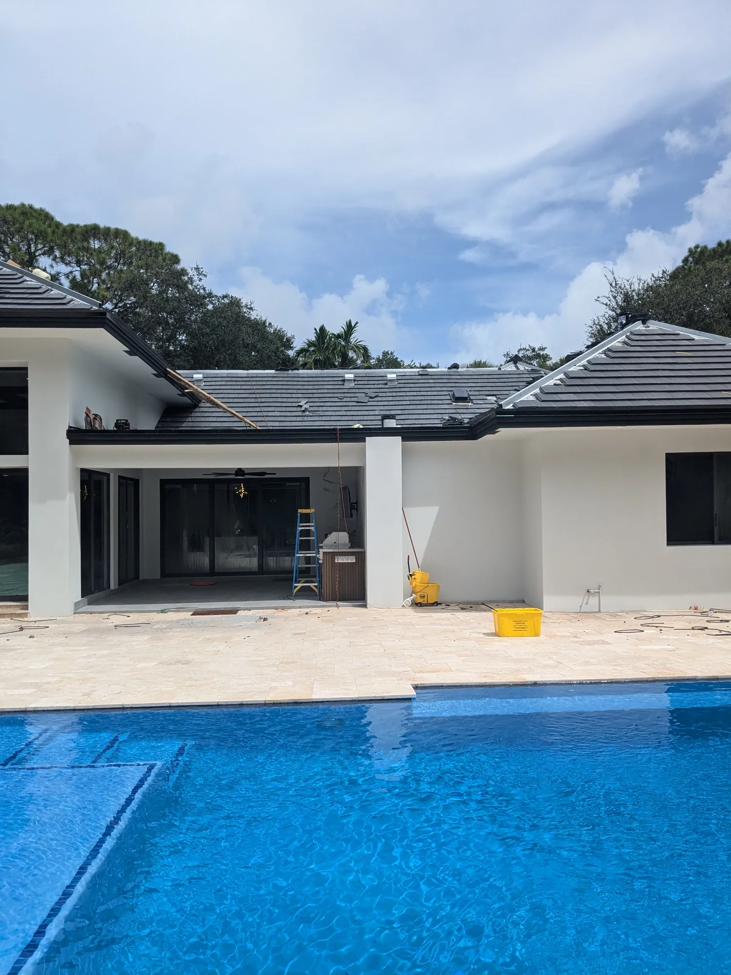 Finished charcoal flat tile roof on a luxury South Florida home with pool, ladders and tools staged at completion by DR Construction & Roofing